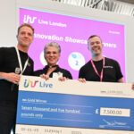"Three people smiling on stage at IHR Live London 2025, holding a large cheque for £7,500 awarded to the Gold Winner of the Innovation Showcase. A bright pink screen behind them displays the event logo and award title."